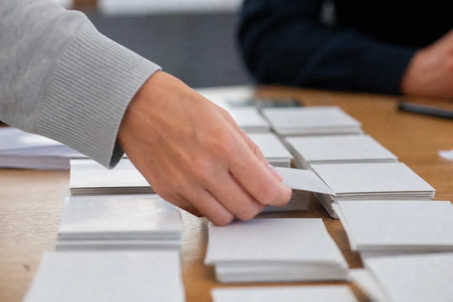 Des fiches cartonnées réparties en colonnes, une main en retirant une.