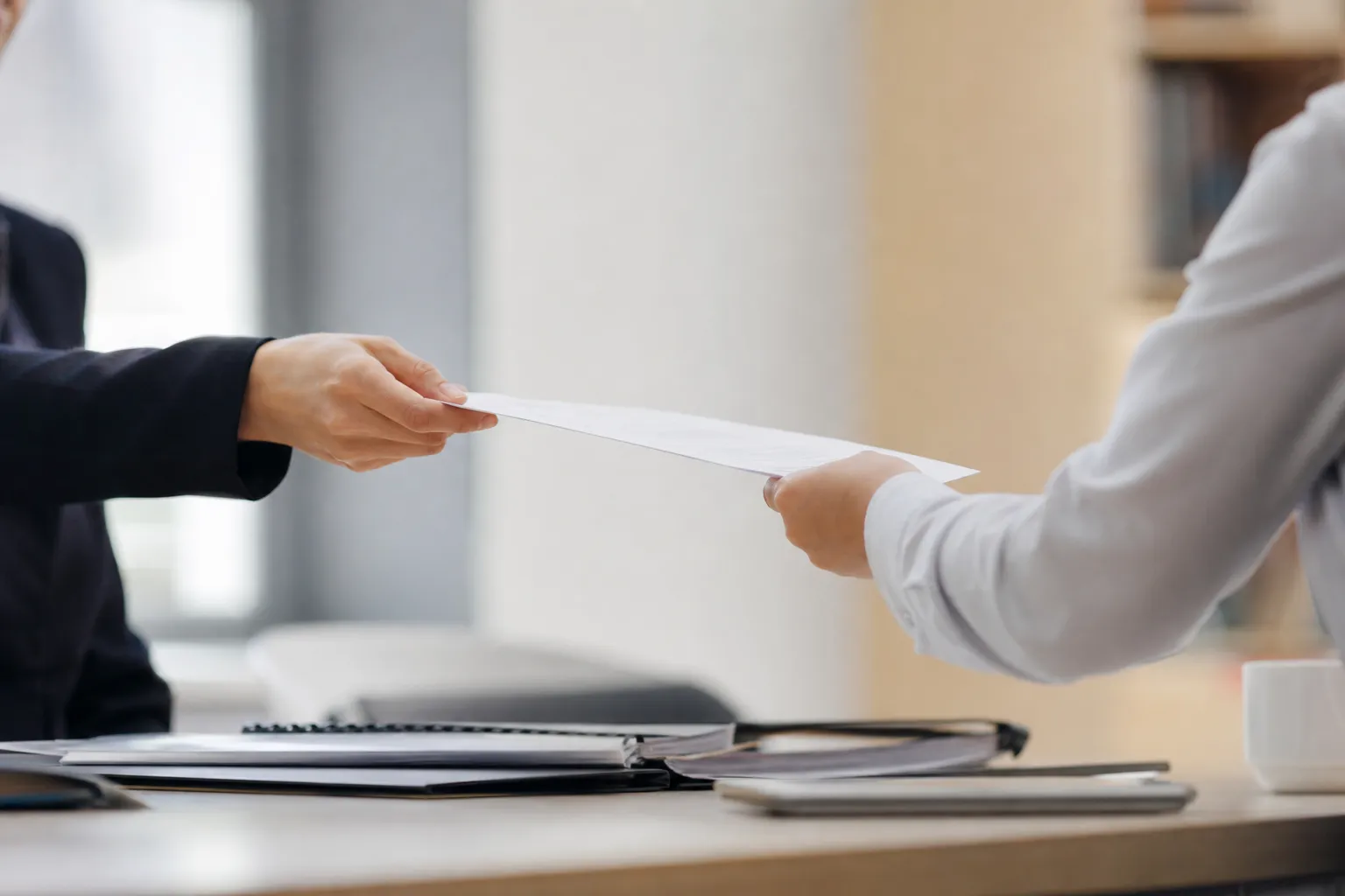 Un document tendu d'une main à une autre au-dessus d'un bureau.