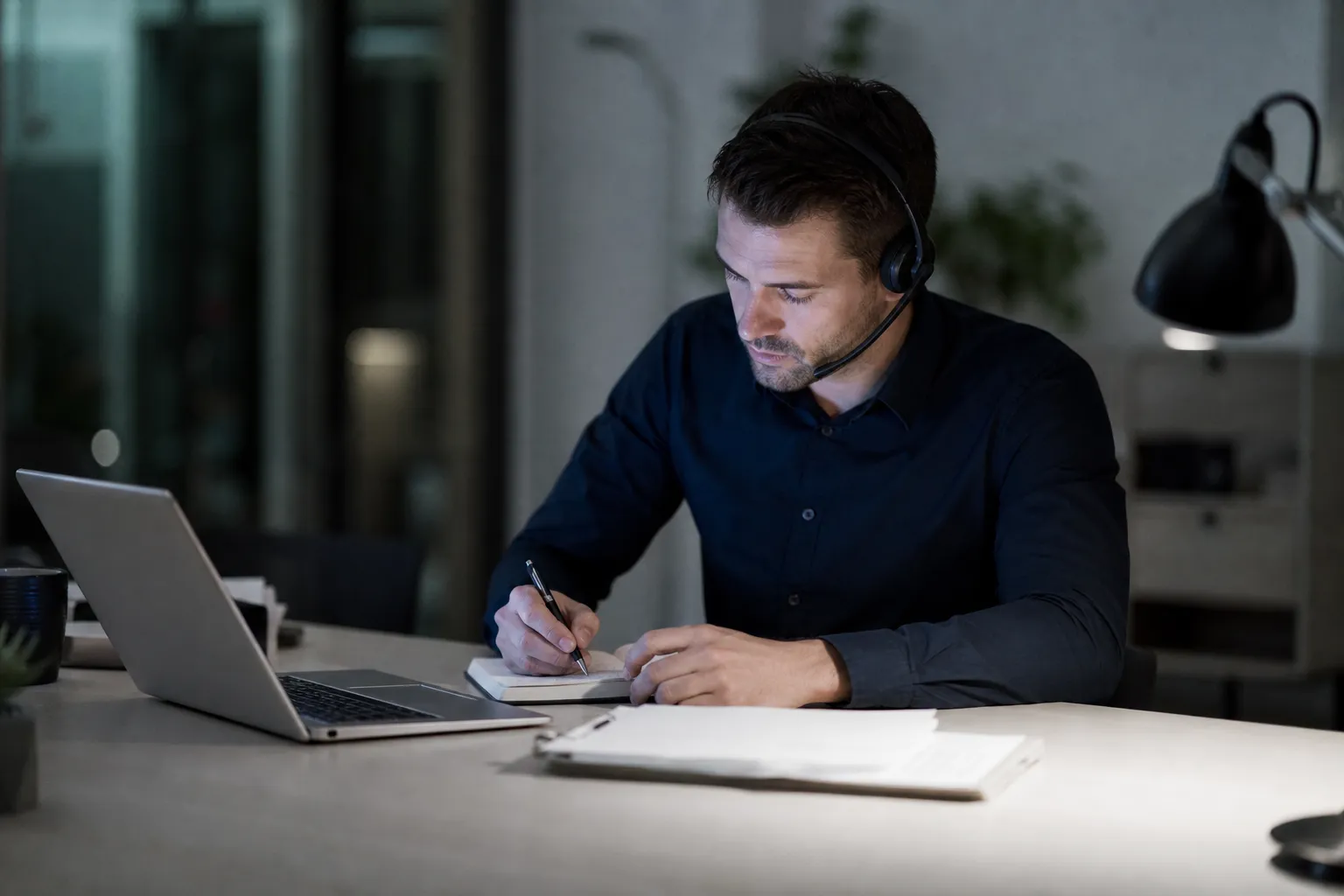 Une personne en appel, casque léger, regard baissé sur ses notes manuscrites.